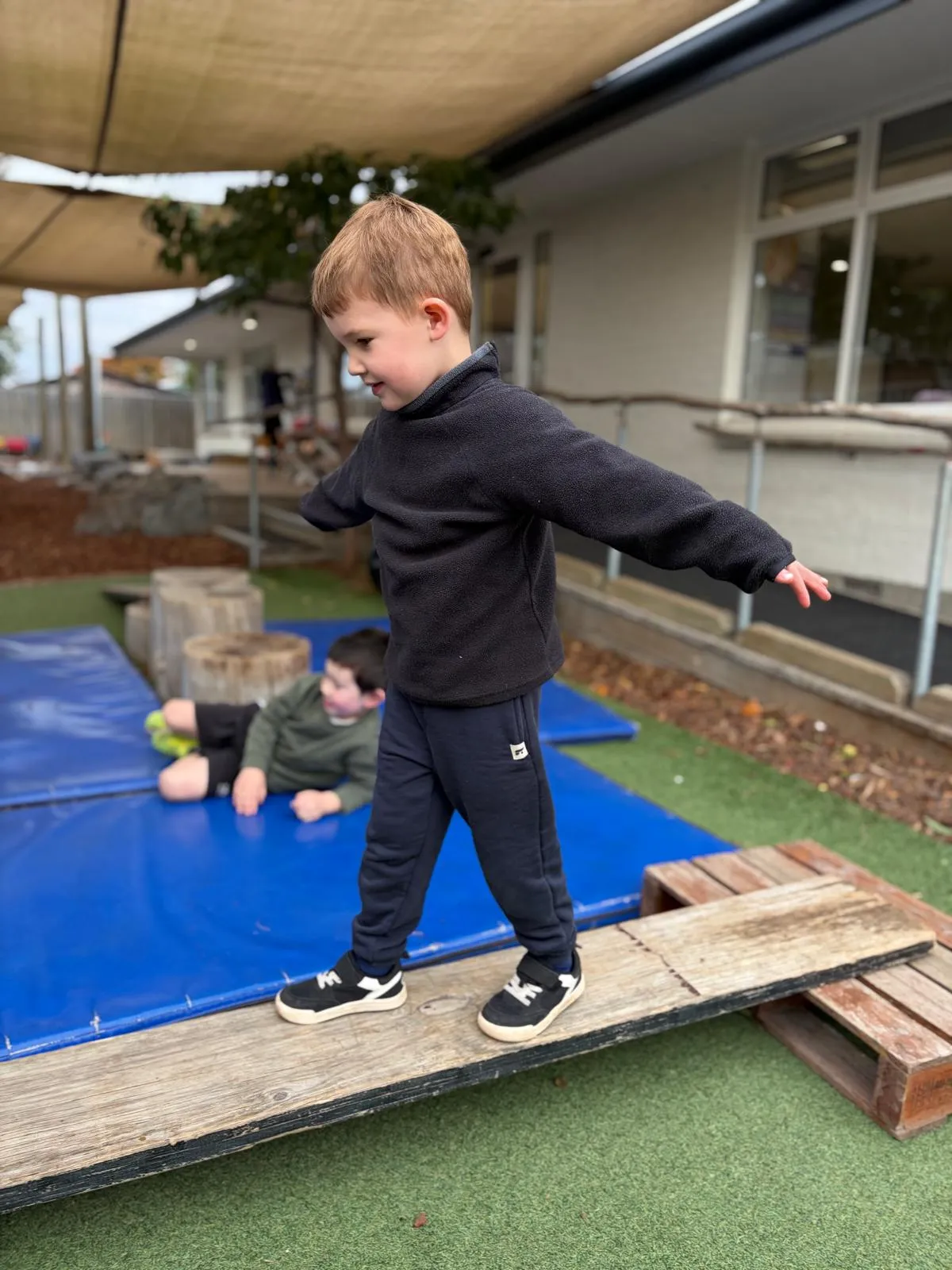 A child balancing along the wooden plank outside with arms out wide