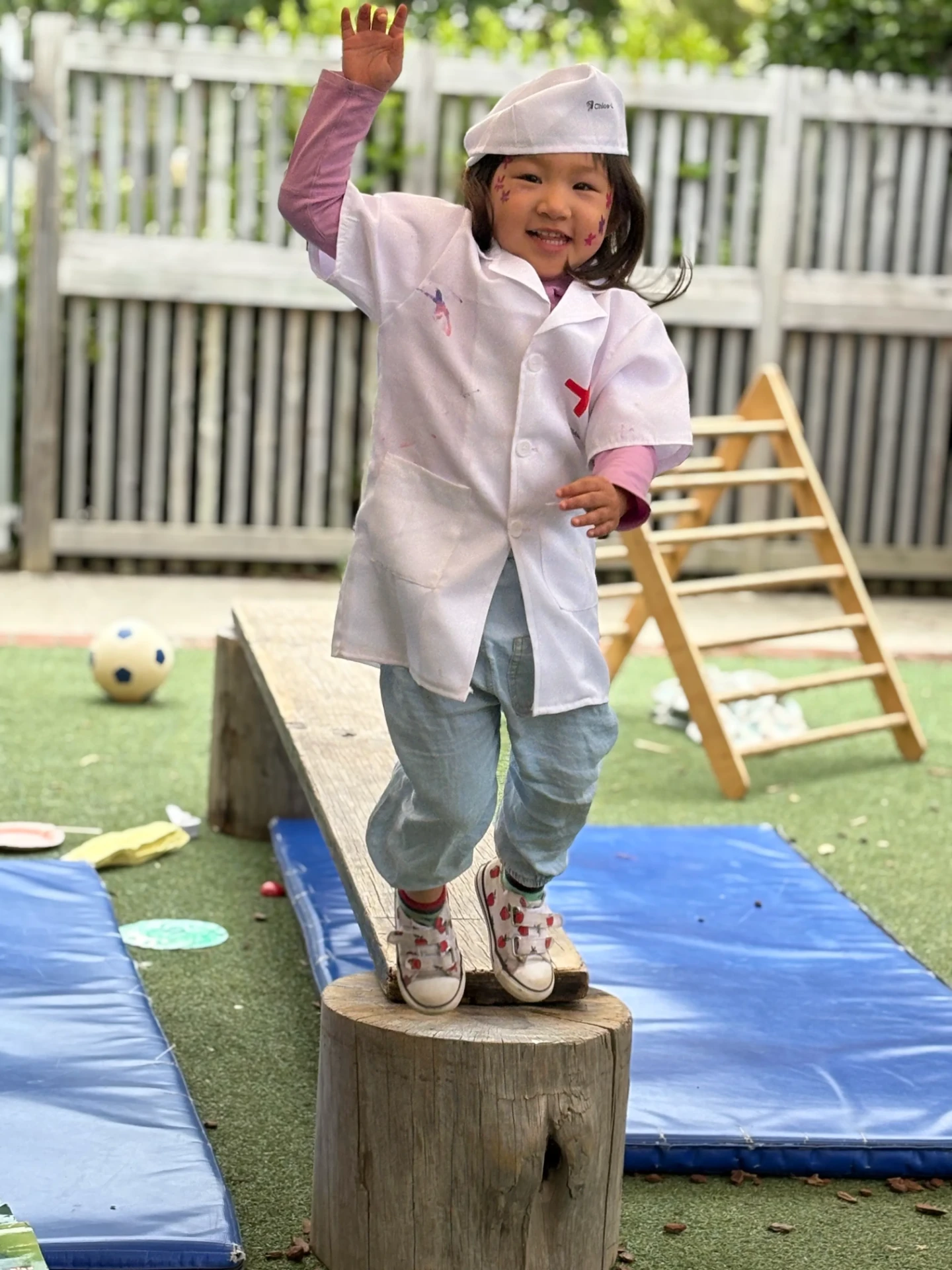 A smiling child in dress ups waving while balancing on a log stump at Wonderhub